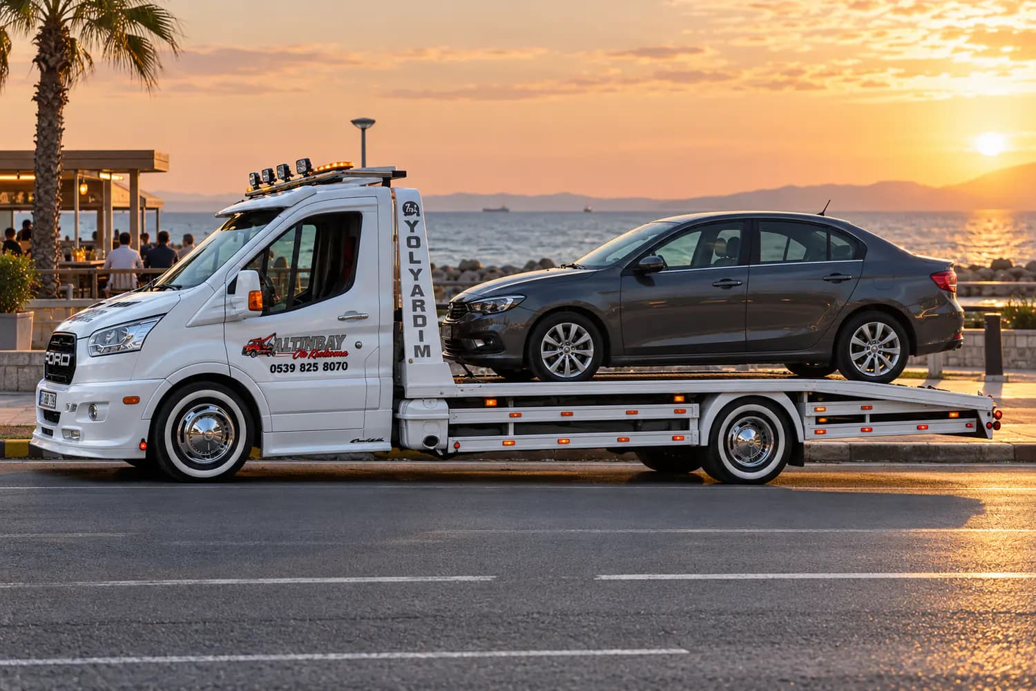 Beyaz bir kayar kasalı çekicinin sahil yolu kenarında otomobili yüklemesi
